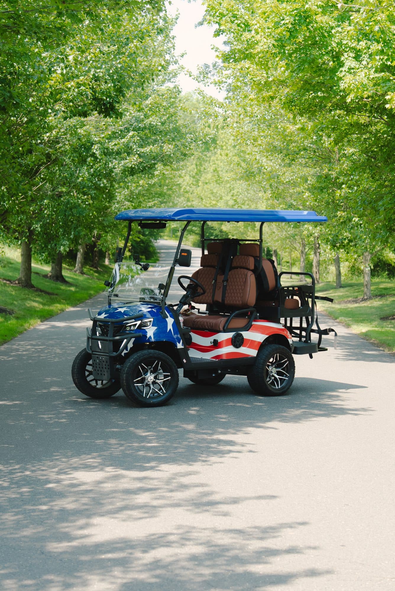 EA4R+ four-seat golf cart in an American flag custom wrap with a blue roof and brown seats on a tree-lined road
