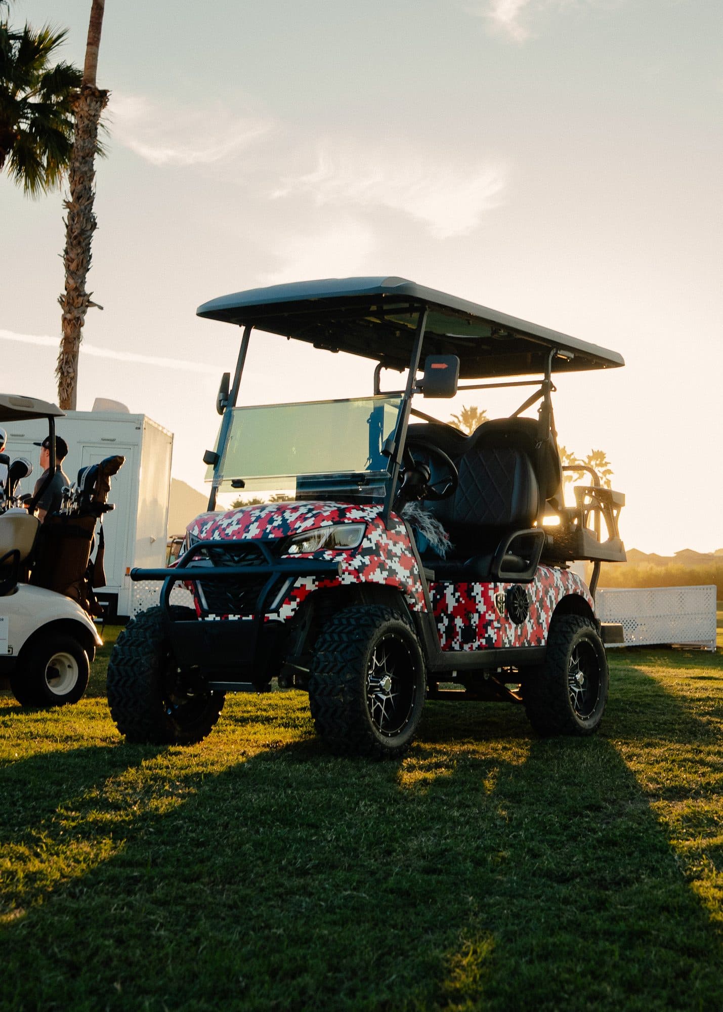 EA4R+ four-seat golf cart in a red, black and white digital camo custom wrap with black seats at sunset