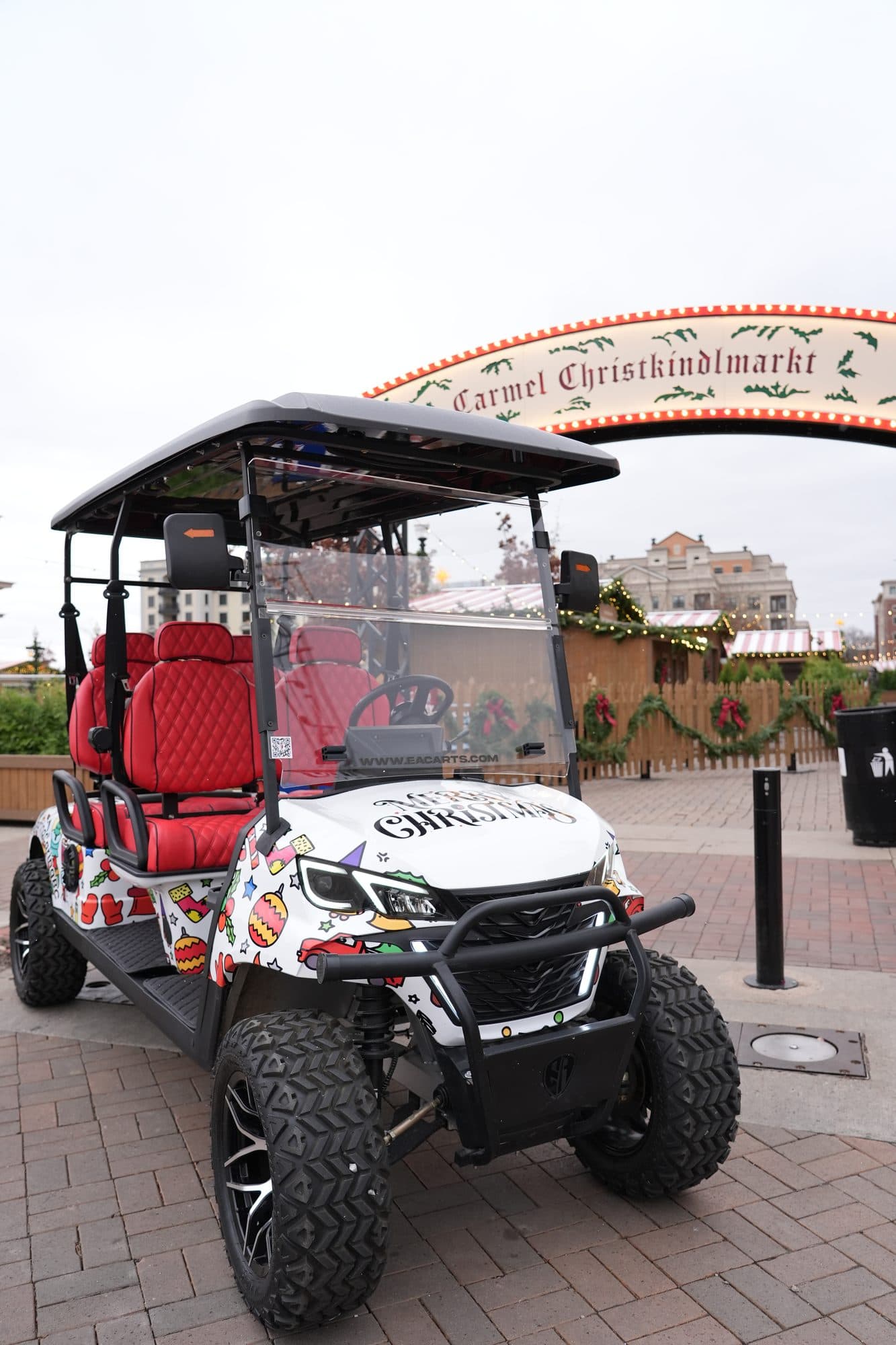 EA6R+ six-seat golf cart in a white Christmas custom wrap with red quilted seats under the Carmel Christkindlmarkt arch