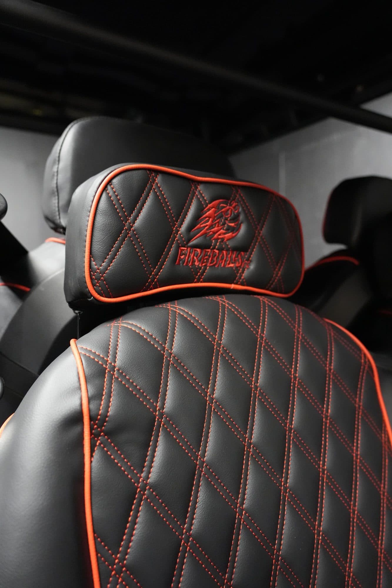 Close-up of a black quilted EA Carts seat with orange piping and stitching and an embroidered Fireballs logo on the headrest