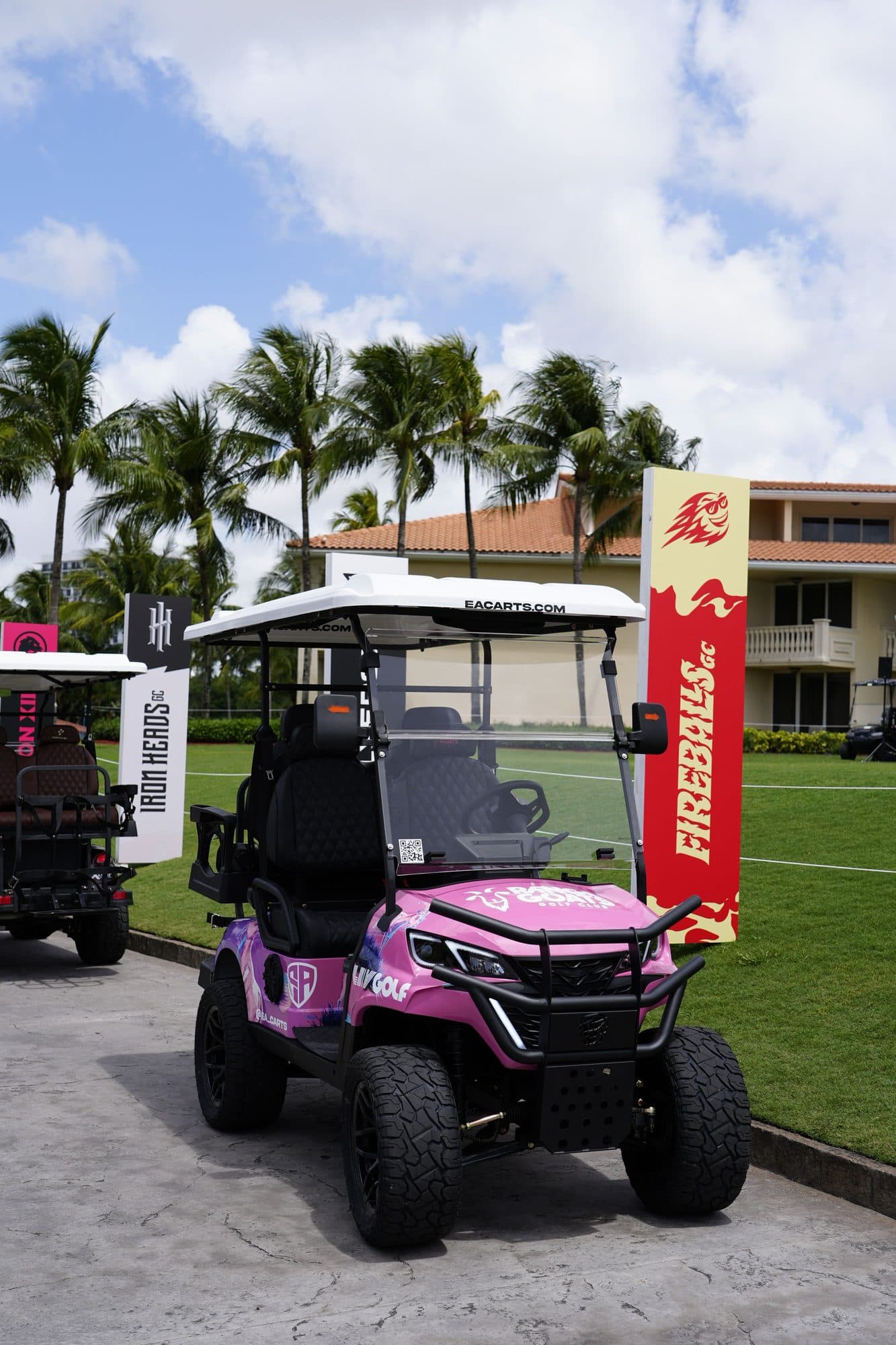 EA Carts golf cart in a pink LIV Golf custom wrap with black seats parked beside team banners