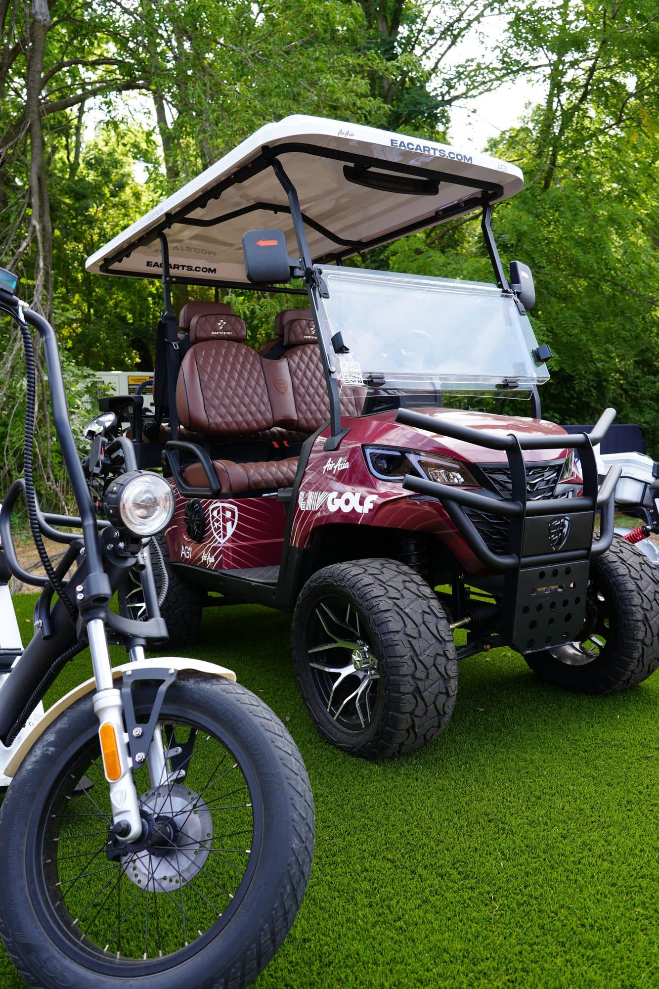 EA Carts golf cart in a maroon LIV Golf custom wrap with quilted seats on grass, an EA Golf Bike beside it
