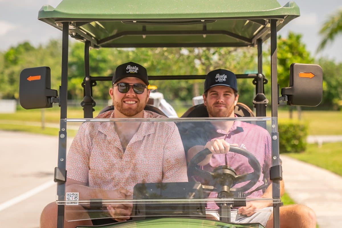 Two adults in Busta Jack caps in a green EA Carts golf cart with a green roof, front view