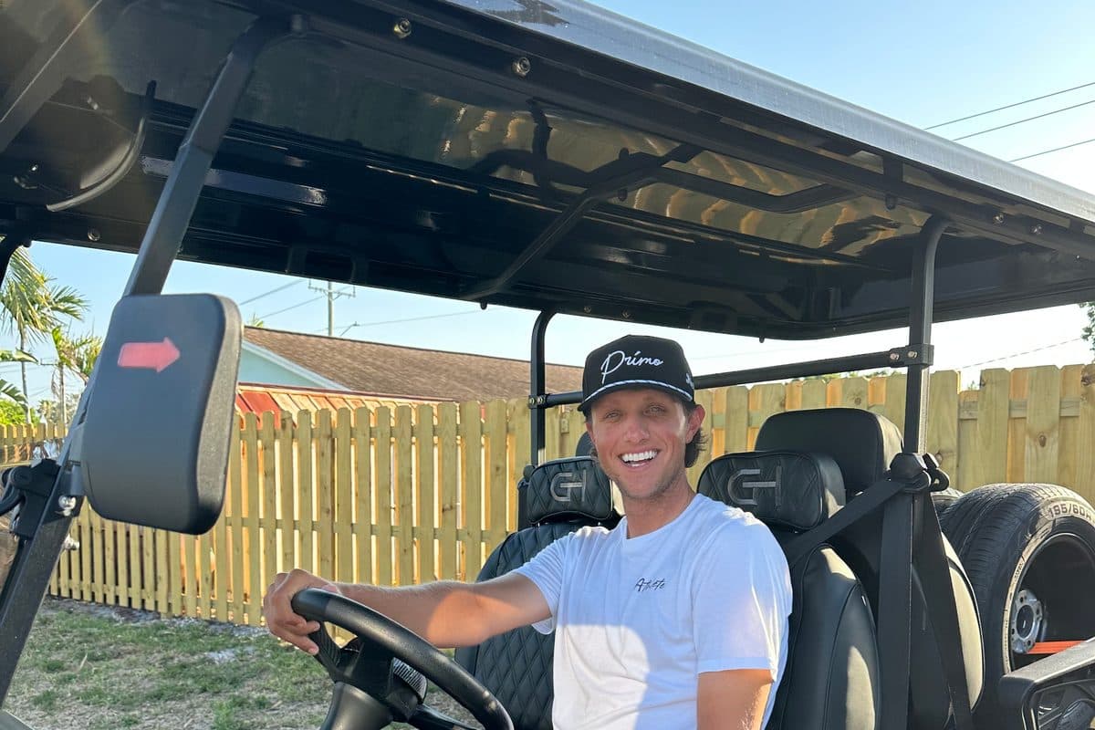 Smiling adult at the wheel of a black EA Carts golf cart with black quilted seats