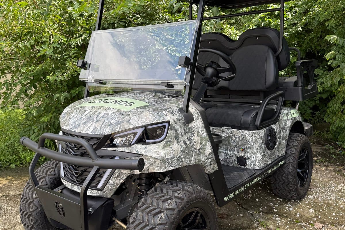 EA Carts golf cart in a gray and white custom camo wrap with a Legends decal and black seats, parked by green shrubs