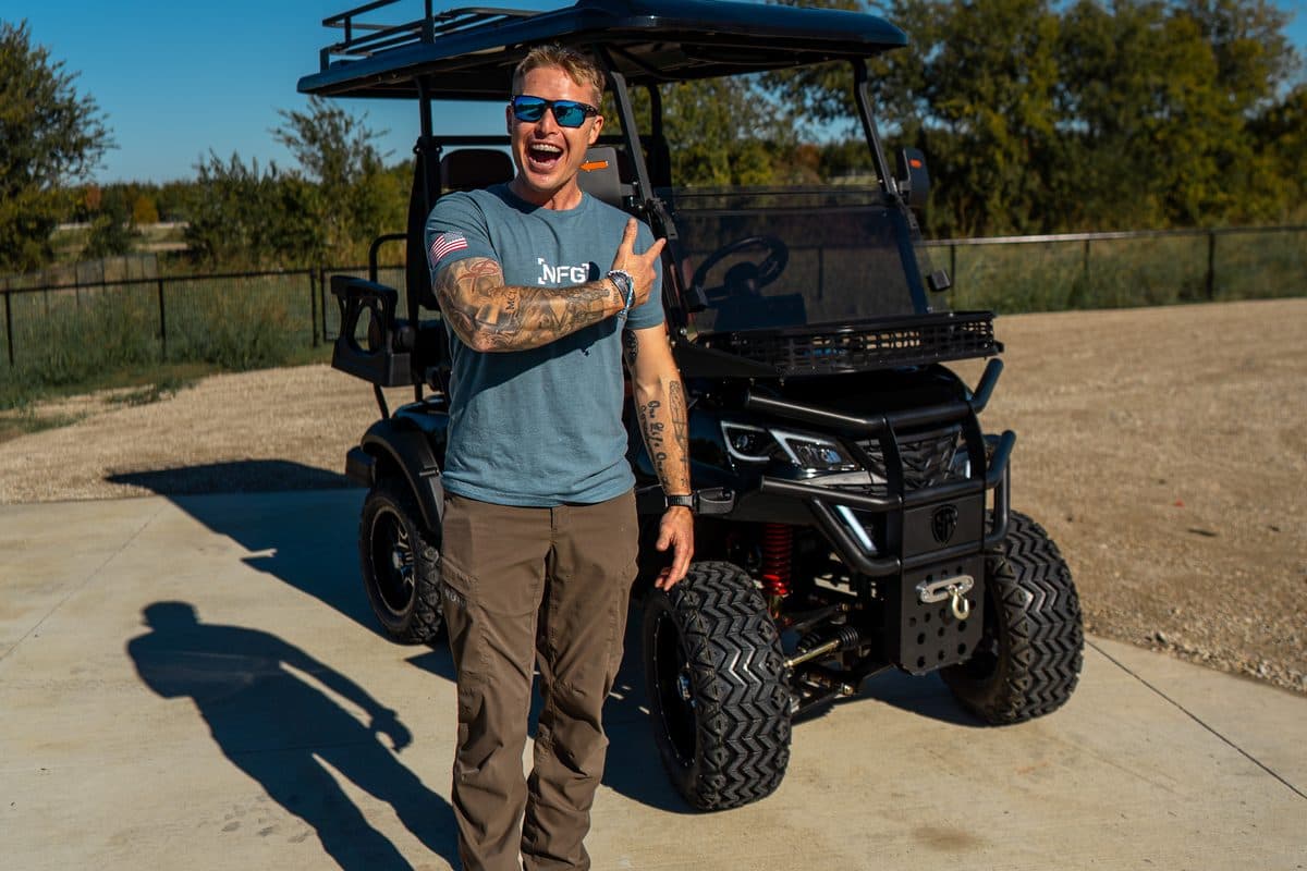 Smiling adult pointing at a black EA Carts cart with roof rack and brush guard parked on a concrete pad