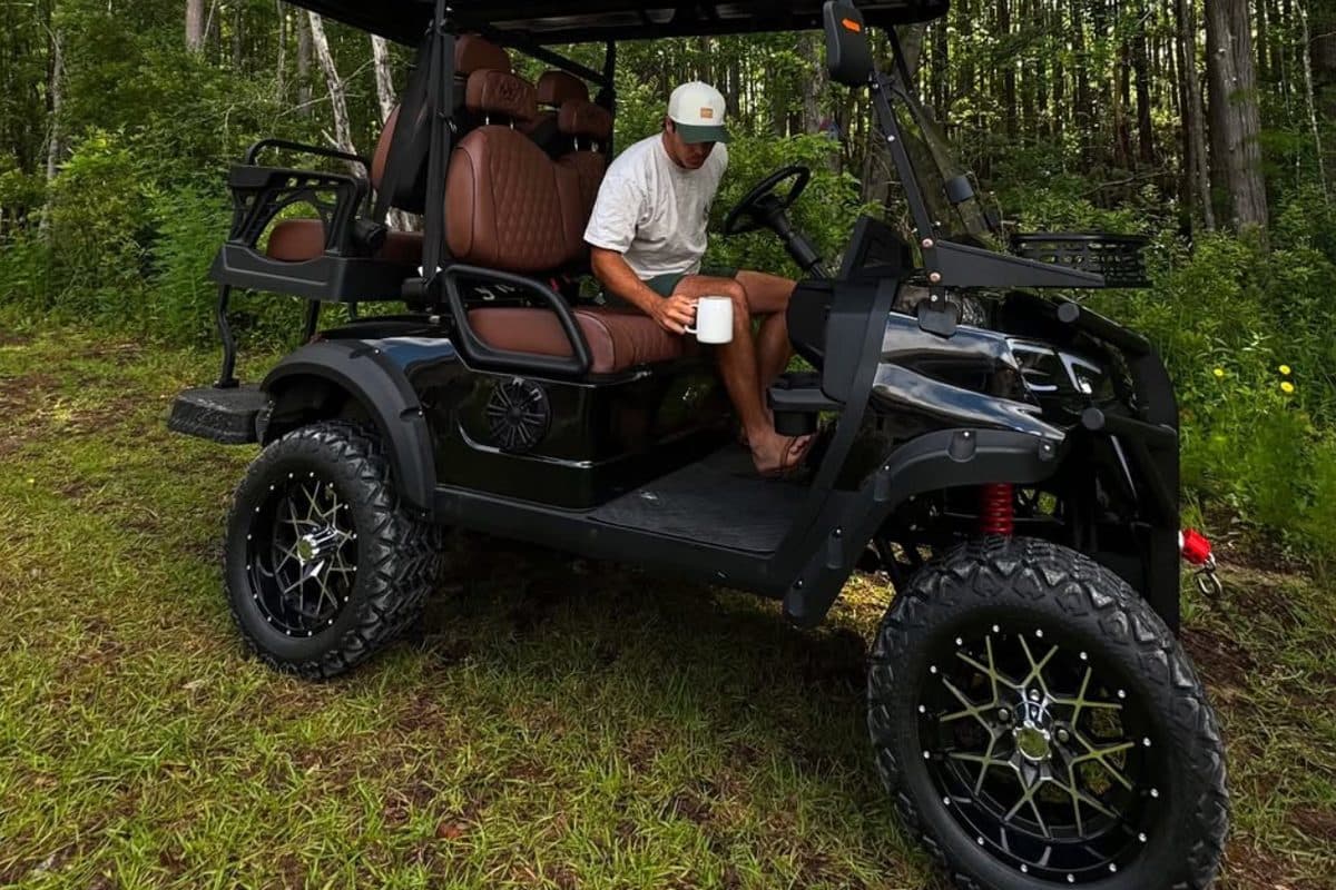 Adult with a coffee mug seated in a black EA4X4 with brown quilted seats in a green forest