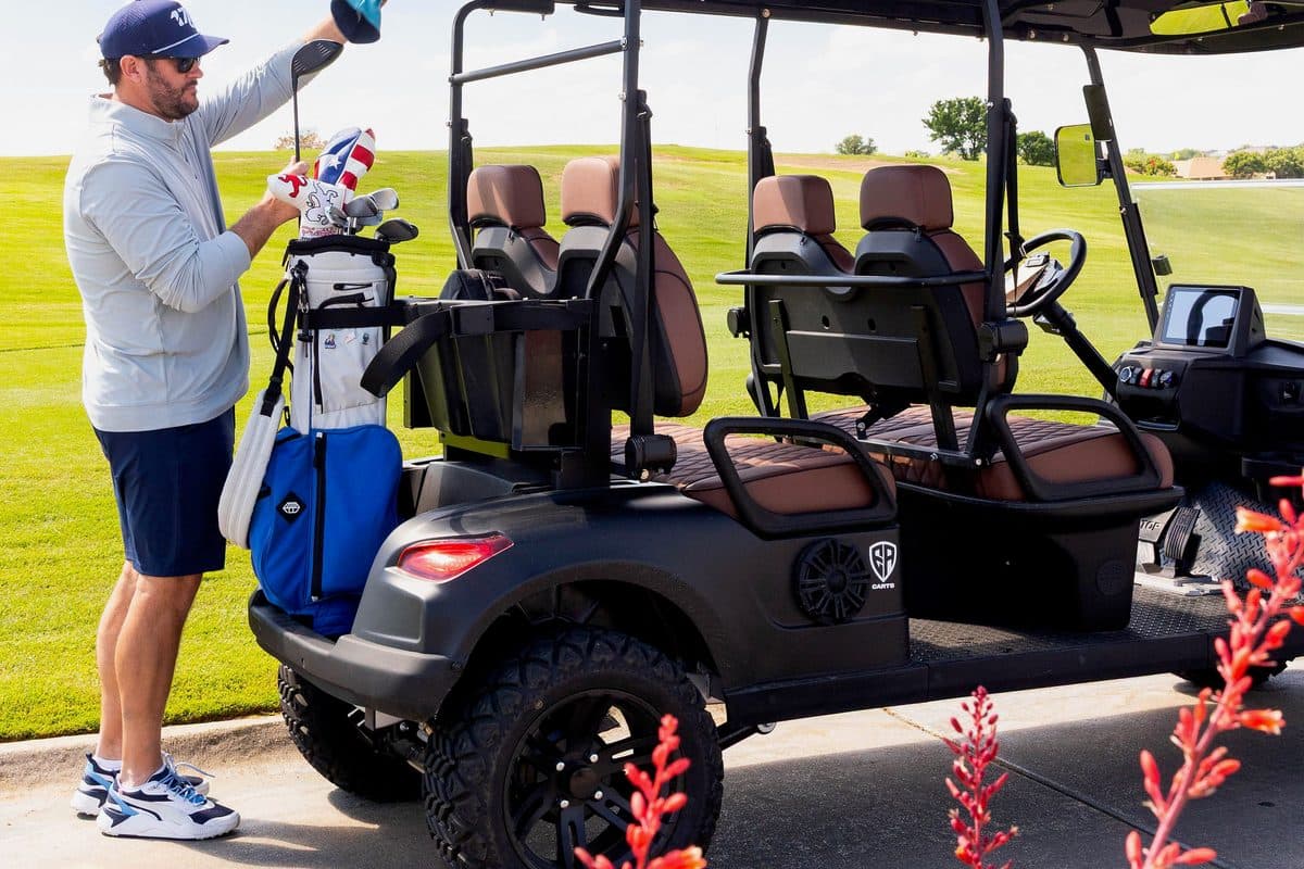 Golfer lifting a club from a golf bag on the back of a black EA Carts golf cart with brown seats