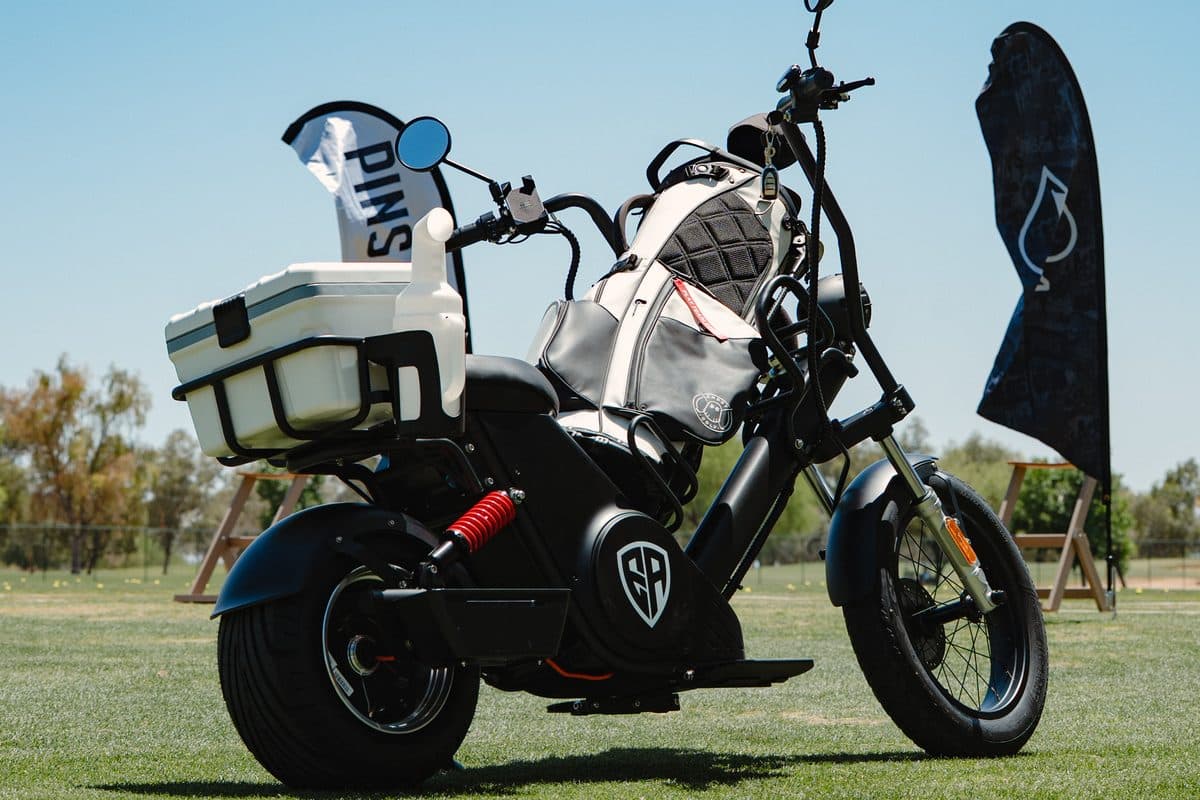 Black EA Golf Bike with a white golf bag, white cooler and a small Pins flag, parked on grass