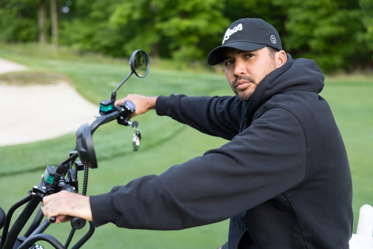 Adult in a black Lads cap and hoodie at the handlebars of an EA Golf Bike on a golf course