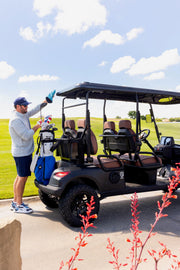 Man standing next to a EA4F+ golf cart on a golf course with a clear sky.